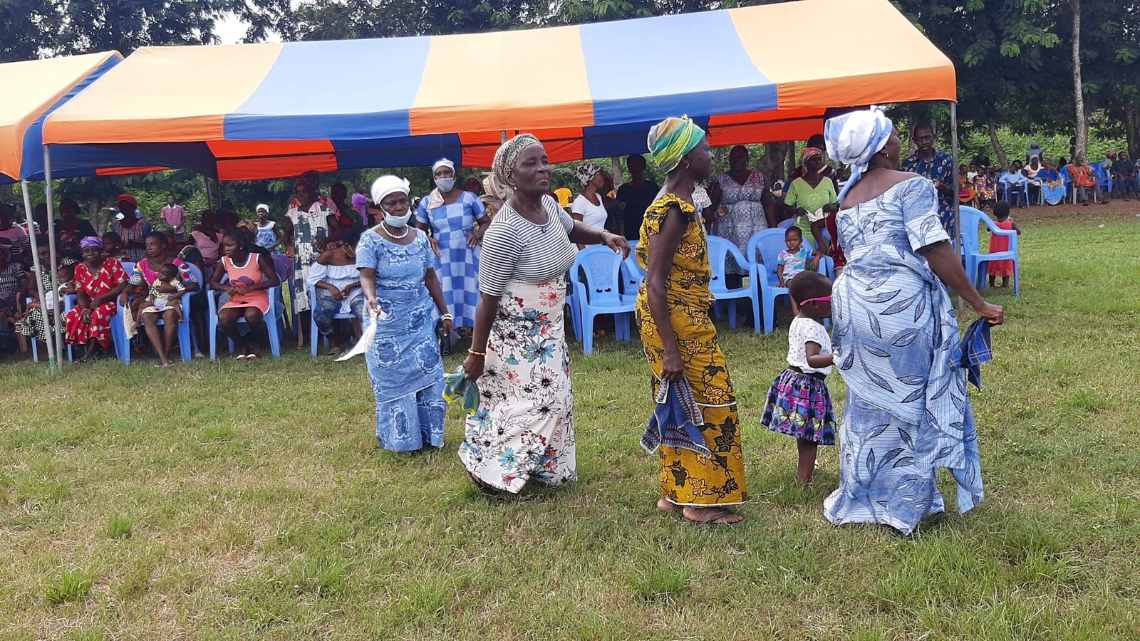 Women in bright dress dancing at a community celebration in rural Ghana.